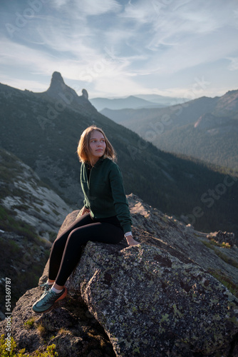 Young beautiful girl tourist sits on stone in mountains after climbing rock