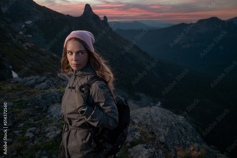 Young beautiful girl tourist with backpack in mountains in late evening after climbing rock