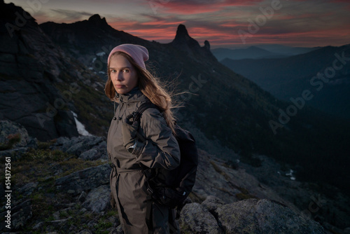 Young beautiful girl tourist with backpack in mountains in late evening after climbing rock