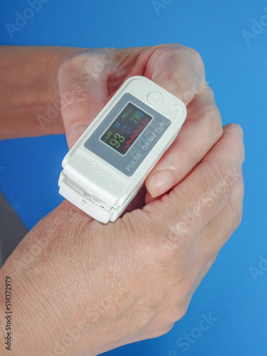 Woman using fingertip pulse oximeter on blue background, top view