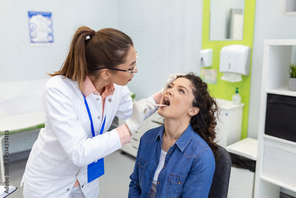 Female patient opening her mouth for the doctor to look in her throat. Otolaryngologist examines sore throat of patient.