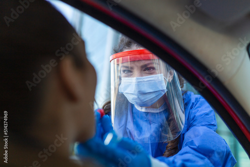 Medical worker performing drive-thru COVID-19 check,taking nasal swab specimen sample from female patient through car window,PCR diagnostic for Coronavirus presence,doctor in PPE holding test kit photo
