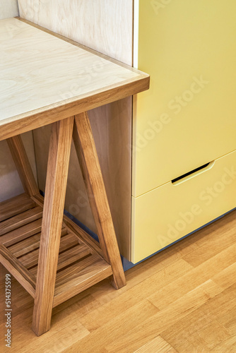 Fragment of children table with cabinet made of plywood and solid oak stands near yellow cabinet. Wooden furniture for bedroom interior closeup