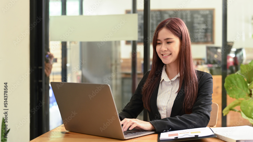 Happy young working woman looking at screen, typing email on computer laptop at workplace Happy young working woman looking at screen, typing email on computer laptop at workplace