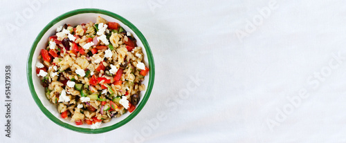 Banner. Multi-colored Orzo salad on the table. Tomatoes, cucumbers, feta cheese, olives, red onions, sweet peppers and risoni pasta. Healthy food concept. Horizontal orientation. copy space. Top view. photo