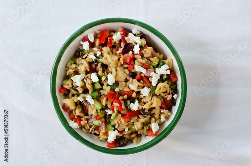 Multi-colored Orzo salad on the table. Tomatoes, cucumbers, feta cheese, olives, red onions, sweet peppers and risoni pasta. Healthy food concept. Horizontal orientation. copy space. Top view.