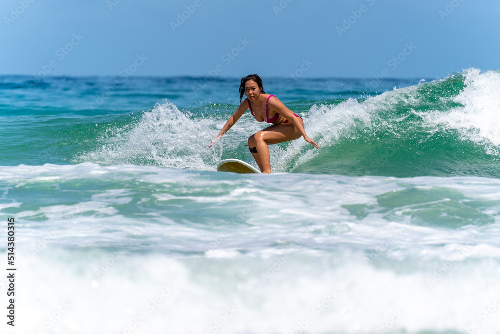 Asian woman surfer surfing and riding surfboard the wave in the sea at tropical beach in sunny day. Healthy female enjoy outdoor activity lifestyle and water sport exercise surfing on summer vacation Asian woman surfer surfing and riding surfboard the wave in the sea at tropical beach in sunny day. Healthy female enjoy outdoor activity lifestyle and water sport exercise surfing on summer vacation
