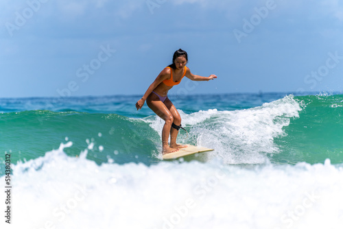 Canvas Print Asian woman surfer surfing and riding surfboard  the wave in the sea at tropical beach in sunny day