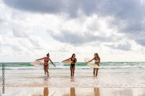 Canvas Print Group of Asian woman surfer in swimwear holding surfboard walking together on tropical beach at summer sunset