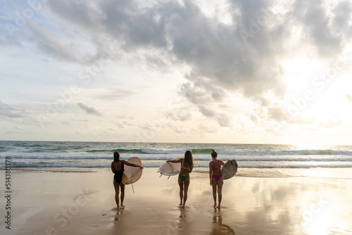 Canvas Print Group of Asian woman surfer in swimwear holding surfboard walking together on tropical beach at summer sunset