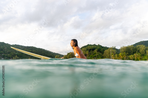 Photography Asian woman surfer paddling surfboard and riding the wave in the sea at tropical beach at summer sunset
