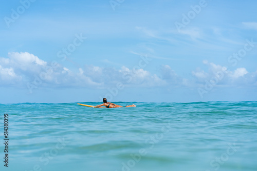 Asian woman surfer surfing and riding surfboard the wave in the sea at tropical beach in sunny day. Healthy female enjoy outdoor activity lifestyle and water sport exercise surfing on summer vacation