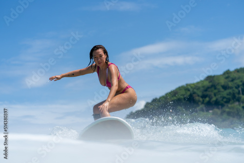Canvas Print Asian woman surfer surfing and riding surfboard the wave in the sea at tropical beach in sunny day