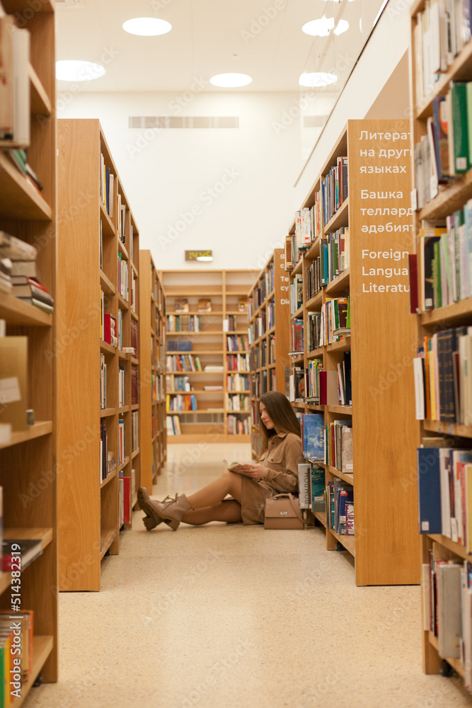 Young woman sitting at the library holding book. millennial reading books, standing between bookshelves in the bookstore. Studying at university library. College or higher education lifestyle concept. Young woman sitting at the library holding book. millennial reading books, standing between bookshelves in the bookstore. Studying at university library. College or higher education lifestyle concept.