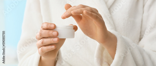 Young woman applying cosmetic cream onto her hands, closeup