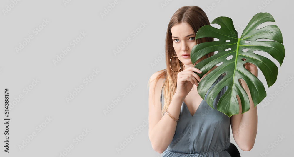 Portrait of beautiful woman with green tropical monstera leaf on light background with space for text Portrait of beautiful woman with green tropical monstera leaf on light background with space for text