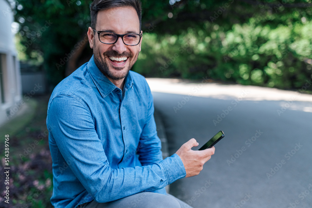 Portrait of cheerful businessman using smart phone while sitting by the road Portrait of cheerful businessman using smart phone while sitting by the road