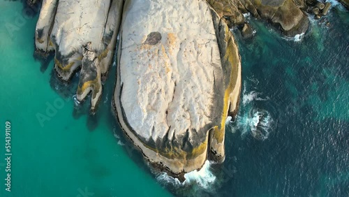 blue ocean waves crashing on large boulders at Llandudno Beach in Cape Town, top down aerial