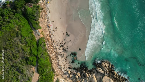 top down view of rocky coastline and turquoise blue ocean waves on pristine white sand Llandudno Beach in Cape Town, aerial