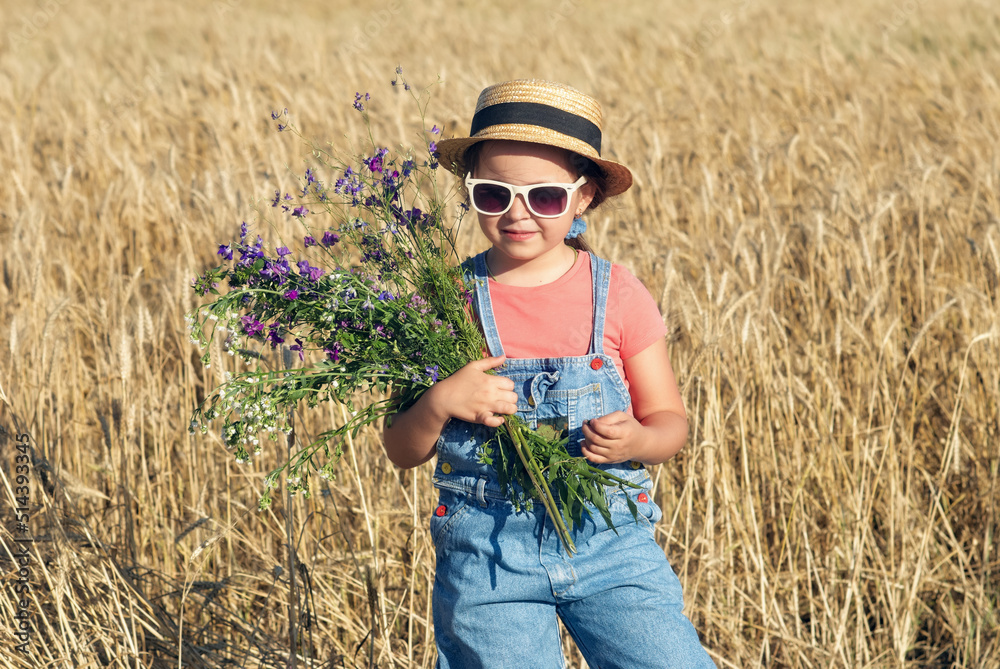 Beautiful little girl in a straw hat and sunglasses in a wheat field
