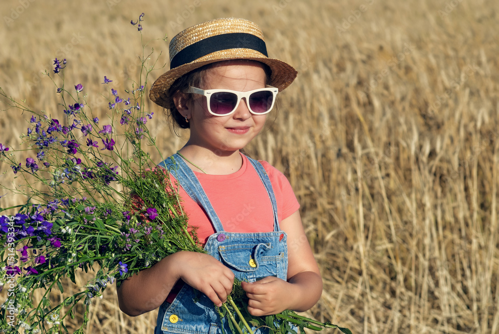 Beautiful little girl in a straw hat and sunglasses in a wheat field