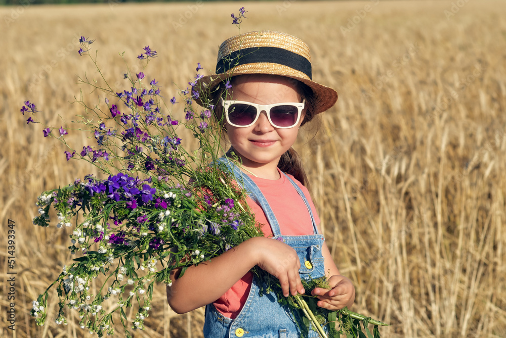 Beautiful little girl in a straw hat and sunglasses in a wheat field