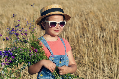 Obraz na płótnie Beautiful little girl in a straw hat and sunglasses in a wheat field w salonie
