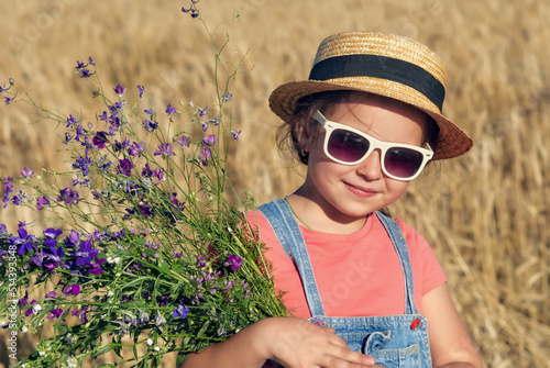 Obraz na płótnie Beautiful little girl in a straw hat and sunglasses in a wheat field w salonie