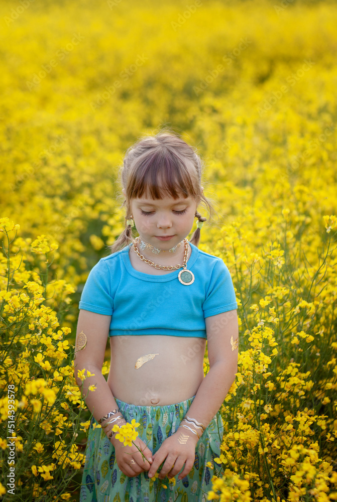 Pretty little girl walking with blue dress in boho style in rapeseed field. Cute young lady model in summer sunny day. Pretty little girl walking with blue dress in boho style in rapeseed field. Cute young lady model in summer sunny day.