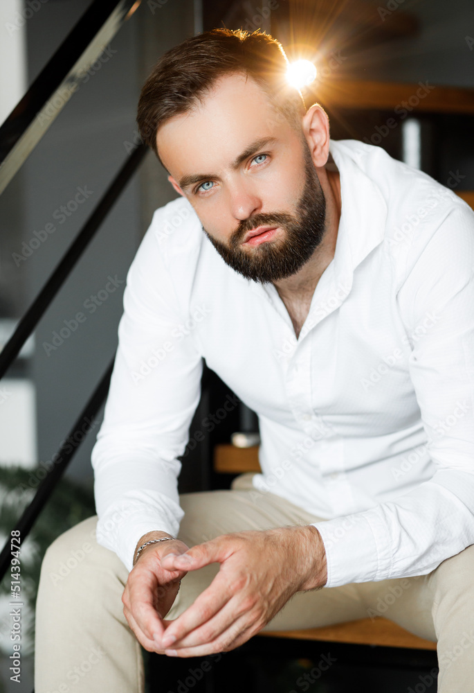 A handsome gentleman in a beige suit sits on the stairs in a stylish interior.
A handsome gentleman in a beige suit sits on the stairs in a stylish interior.