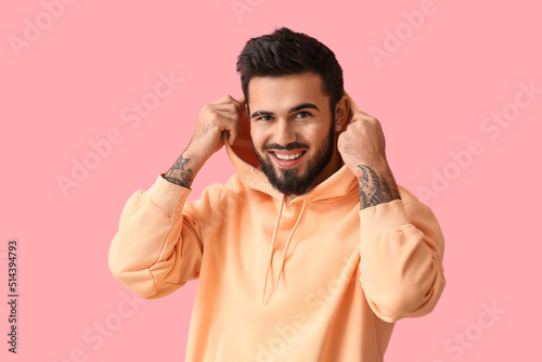 Fashionable bearded man wearing hoodie on pink background