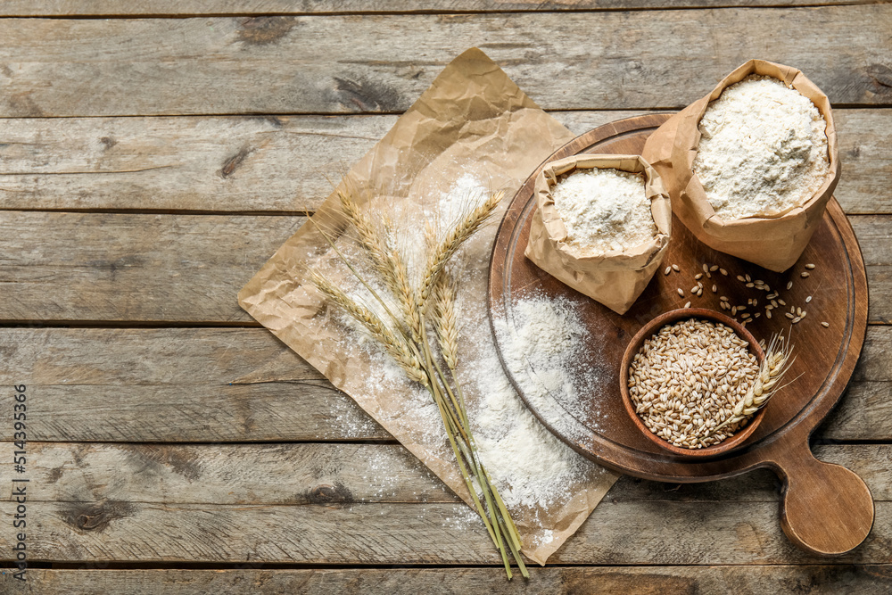 Wheat ears, bowl, paper bags with flour, board and parchment paper on wooden background Wheat ears, bowl, paper bags with flour, board and parchment paper on wooden background