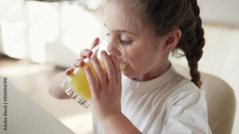 girl child drinking juice. happy family a healthy eating kid dream concept. daughter girl drinking yellow juice from a glass cup in the kitchen. indoor child drinking fruit juice girl child drinking juice. happy family a healthy eating kid dream concept. daughter girl drinking yellow juice from a glass cup in the kitchen. indoor child drinking fruit juice