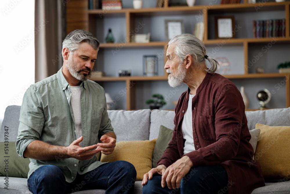 Obraz premium Fathers day. Adult son visiting senior father.Two generations family enjoy pleasant conversation,talking, sharing news,spending time together sitting on couch at home. Understanding, care and support.