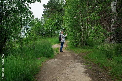 Male tourist stands on a forest road and shoots a video in a natural park in the north of Europe