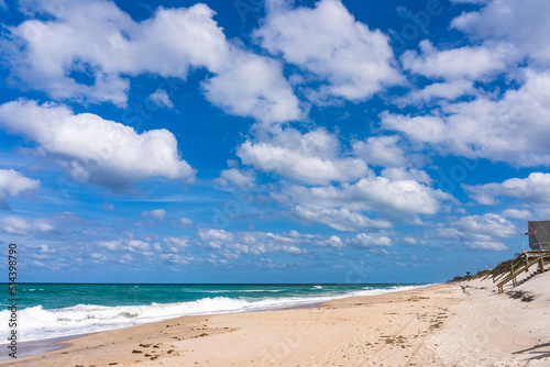 Deserted beach in Florida in stormy sunny weather. Green waves of the ocean, a piercing blue sky with lush white clouds © Sergey + Marina
