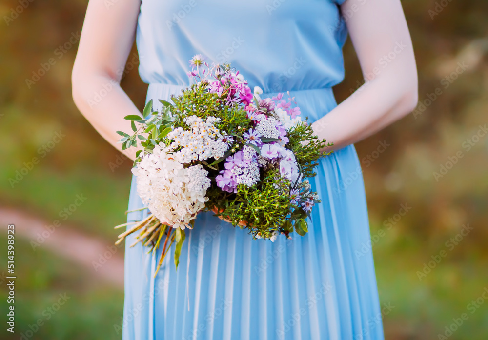 Beautiful young girl in blue dress holding the bouquet of wildflowers in her hands. 
