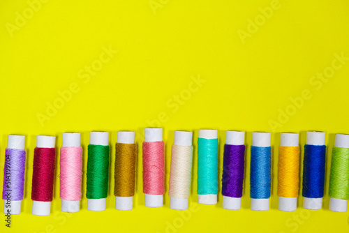 A set of multi-colored threads for sewing with an empty space for text on a yellow background, top view. Tailoring and needlework equipment, tailor banner.