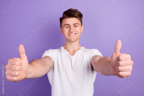 Portrait of cheerful man in basic clothing smiling showing thumbs up at camera isolated over shine background © Tetiana