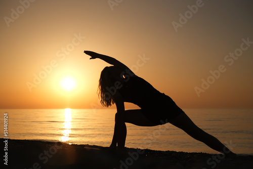 Silhouette of a woman doing yoga on a beach during sunrise