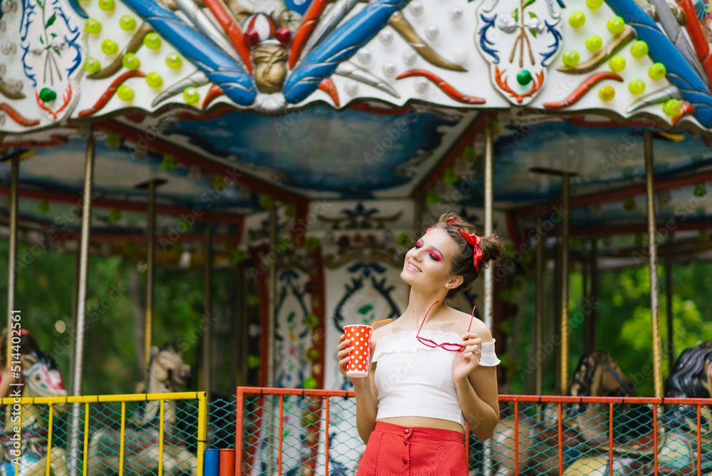 A beautiful young woman walks in an amusement park and holds a paper cup in her hands