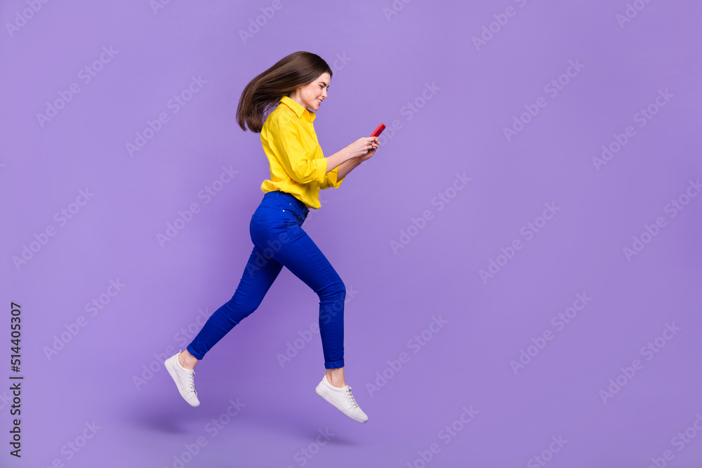 Full length body size view of beautiful trendy cheery girl jumping using device isolated over bright violet purple color background