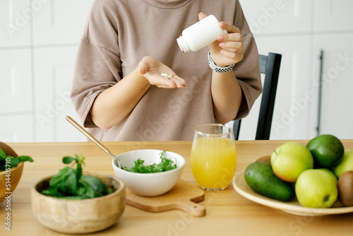 Woman taking vitamins and have healthy breakfast in the kitchen. Healthy lifestyle concept, vitamins, supplements.