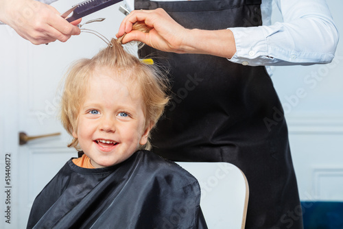 Laughing blond boy get haircut at barbershop by hairstylist