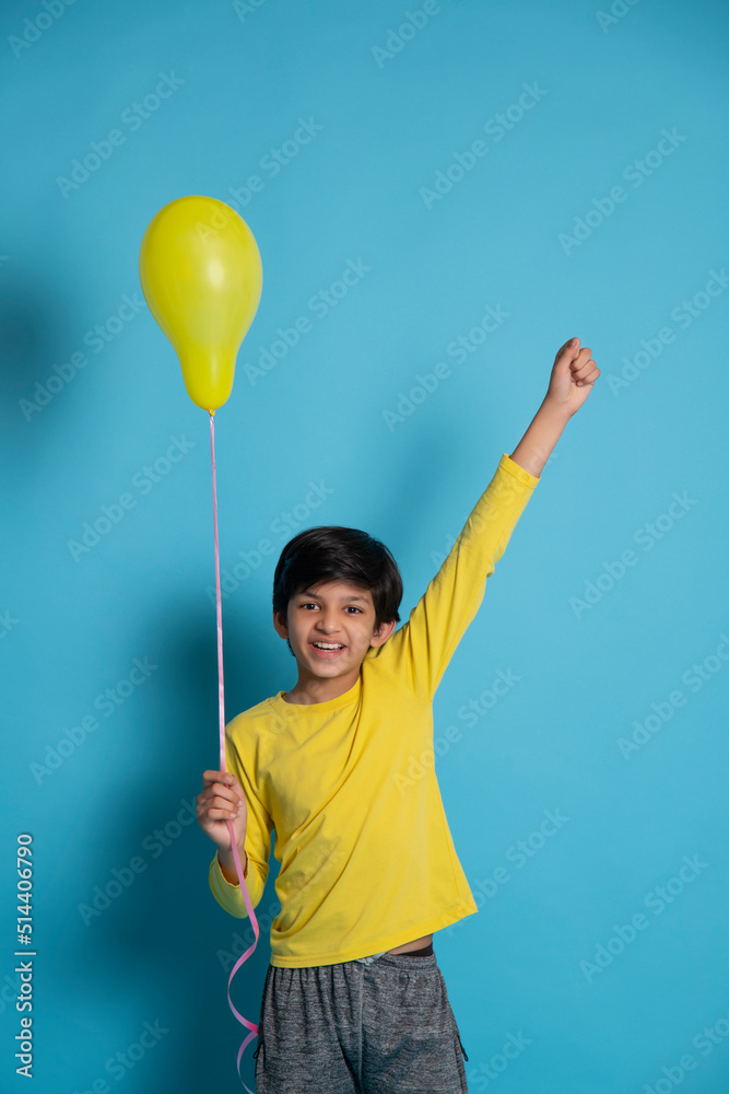 Cheerful boy holding a yellow balloon against blue background Cheerful boy holding a yellow balloon against blue background