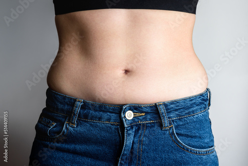Young woman with fat folds on sides on gray background. Overweight concept. View from the stomach.