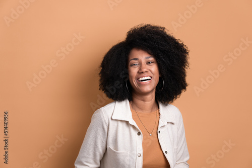 cheerful afro brazilian woman smiling and looking at camera wearing white jacket in beige studio background. portrait, real people concept.