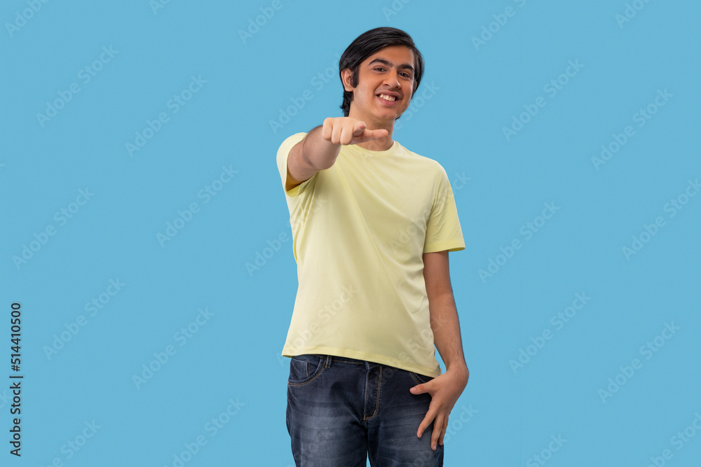 Portrait of a teenage boy pointing towards camera while standing against blue background Portrait of a teenage boy pointing towards camera while standing against blue background