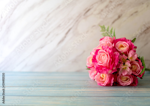 A bouquet of pink roses on the wooden floor and with a marble wall in the background