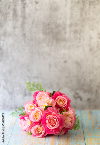 A bouquet of pink roses on the wooden floor and with a cement wall in the background
